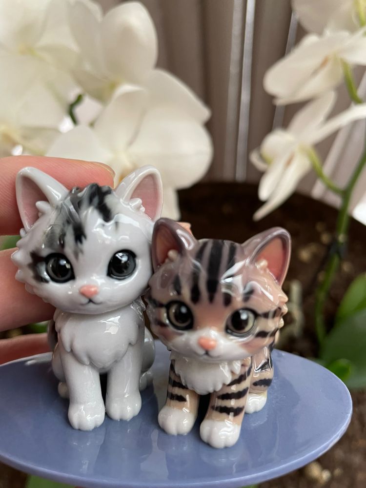 The two finished kitten figurines on one base, held in front of white orchids